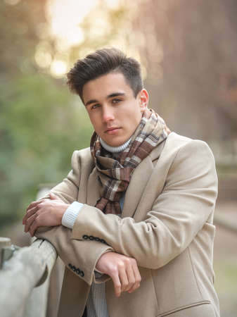 Portrait of a young guy on the street in a coat and scarf.
