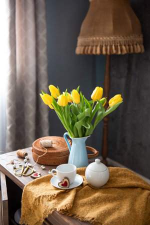 Yellow tulips arranged in vase beside tea set on wooden table with cozy ambianceの写真素材