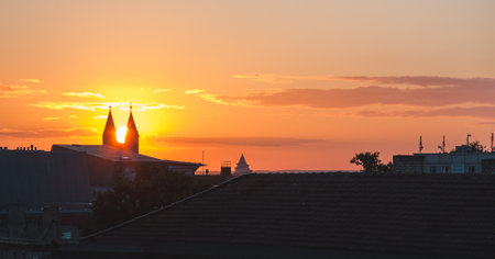 Sunrise over a city while the sun shines through the church towersの写真素材