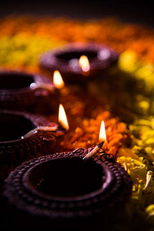 Traditional diya or oil lamp lit on colorful rangoli made up of marigold flower petal, on the...