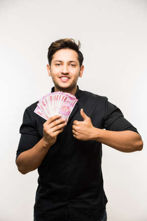 Happy Indian young man holding  new indian currency or 2000 or 500 rupee notes fan, isolated over...