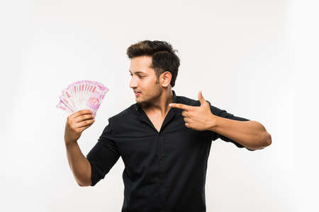 Happy Indian young man holding  new indian currency or 2000 or 500 rupee notes fan, isolated over...