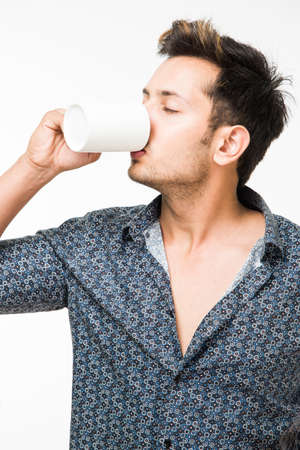 Portrait of a Young handsome Indian man having a cup of coffee, standing isolated over white backgroundの写真素材