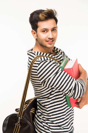 Handsome and young indian Male college student carrying bag on white background while holding college books, laptop or smart phoneの写真素材