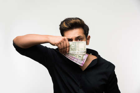 Happy Indian young man holding  new indian currency or 2000 or 500 rupee notes fan, isolated over white backgroundの写真素材