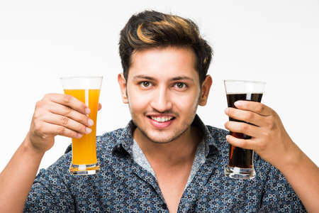 2 glasses : Young handsome Indian man in casual shirt holding two glasses of fresh orange juice and dark aerated drink for breakfast or for refreshment.の写真素材