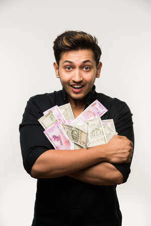 Happy Indian young man holding  new indian currency or 2000 or 500 rupee notes fan, isolated over...