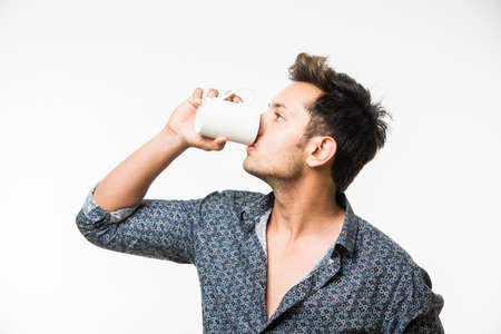 Portrait of a Young handsome Indian man having a cup of coffee, standing isolated over white backgroundの写真素材