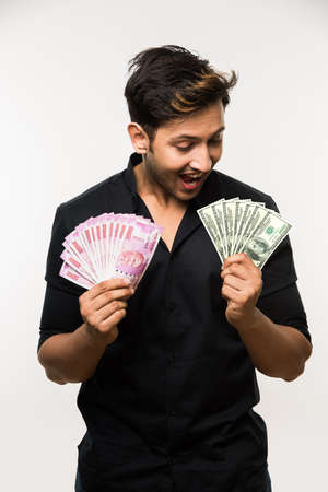 good looking young indian man holding fan of currency notes, Indian 2000 rupee and US dollar 100...