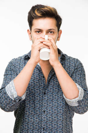 Portrait of a Young handsome Indian man having a cup of coffee, standing isolated over white backgroundの写真素材
