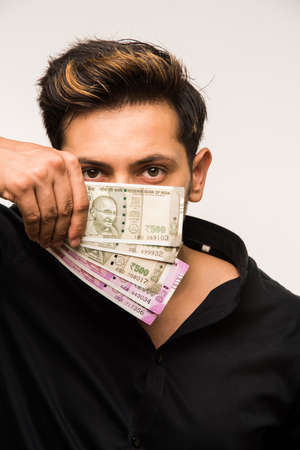 Happy Indian young man holding  new indian currency or 2000 or 500 rupee notes fan, isolated over...