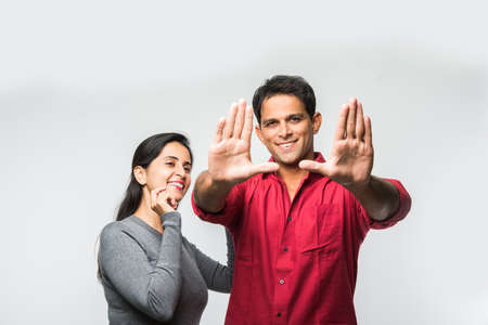 stock photo of Indian smart and cheerful / happy couple indoor, husband composing frame in the newly purchased or rented house and wife accompanying, indian couple and real estate conceptの写真素材