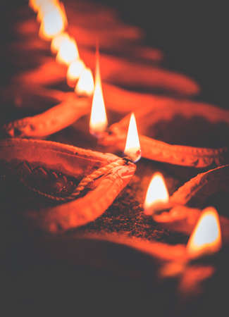 Happy Diwali - many Terracotta diya or oil lamps arranged over clay surface or ground in one line or curved or zigzag form, selective focusの写真素材