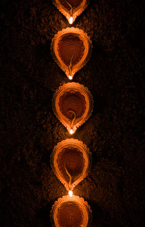 Happy Diwali - many Terracotta diya or oil lamps arranged over clay surface or ground in one line or curved or zigzag form, selective focusの写真素材