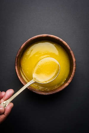 Ghee or clarified butter close up in wooden bowl and silver spoon, selective focusの写真素材