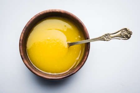 Ghee or clarified butter close up in wooden bowl and silver spoon, selective focusの写真素材