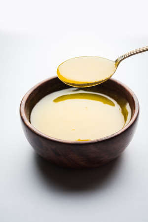 Ghee or clarified butter close up in wooden bowl and silver spoon, selective focus
