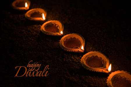 Happy Diwali greeting card design using Beautiful Clay diya lamps lit on diwali night Celebration.  Indian Hindu Light Festival called Diwali, a festival of lightの写真素材