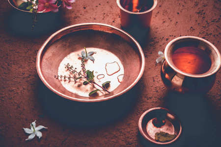 copper kalash, glass, spoon and plate used by Bramhins after sacred thread ceremony while performing Sandhya Vandanam or Sandhya Kriya, over clay background with tulsi or basil leaves & flowersの写真素材
