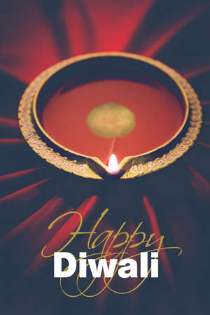 Happy diwali greeting card - Big illuminated diwali diya or clay lamp placed over satin cloth creating rays effect in cloth, moody lighting, selective focusの写真素材