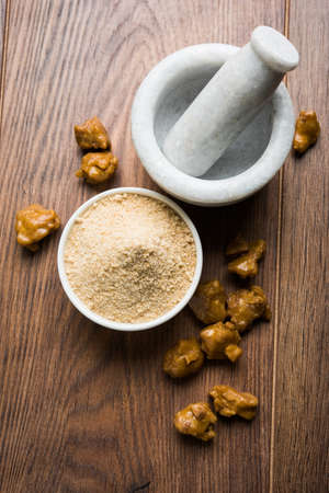 Asafoetida cake and powder or Hing or Heeng which is an important ingredient in Indian food recipes with big wooden spoon and mortar, selective focusの写真素材