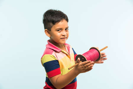 Kite or Patang flying in India, cute and happy little indian boy/kid holding chakri or wooden spindal and standing over blue background on Makar Sankranti Festivalの写真素材