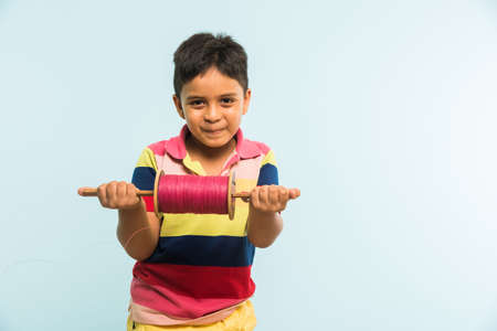 Kite or Patang flying in India, cute and happy little indian boy/kid holding chakri or wooden spindal and standing over blue background on Makar Sankranti Festivalの写真素材