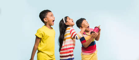 Kite or Patang flying in India, three cute little indian kids enjoying Kite flying in Makar sankranti festival, standing with chakri or wooden spindal and holding thread in excitement on blue backgroundの写真素材