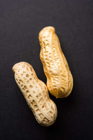 Concept of individuality, luck,value,exclusivity and better choice. Golden peanut or ground nut, standing out amongst normal peanuts, over black or white backgroundの写真素材