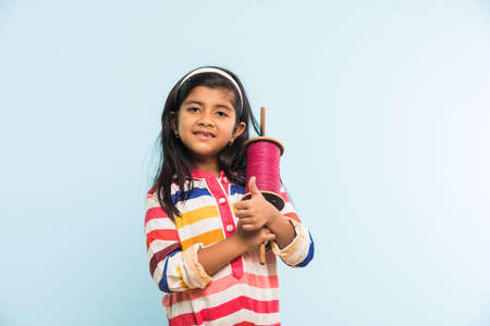 Kite or Patang flying in India, cute and happy little indian girl/female child holding chakri or wooden spindal and standing over blue background on Makar Sankranti Festivalの写真素材