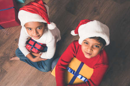 Indian kids celebrating christmas with christmas gifts, decorating christmas tree and having good...