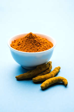 Turmeric powder in ceramic bowl with raw dried turmeric over plain backgroundの写真素材