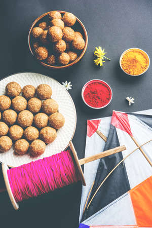 happy Makar Sankranti Festival - Tilgul or Til ladoo in a bowl or plate with haldi kumkum and flowers with Fikri /Reel/Chakri /Spool with colourful thread or manjha and kite over plain backgroundの写真素材