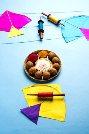 happy Makar Sankranti Festival - Tilgul or Til ladoo in a bowl or plate with haldi kumkum and flowers with Fikri /Reel/Chakri /Spool with colourful thread or manjha and kite over plain backgroundの写真素材