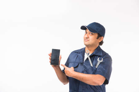 Indian happy auto mechanic in blue suit and cap holding spanner tool in action, isolated over white...