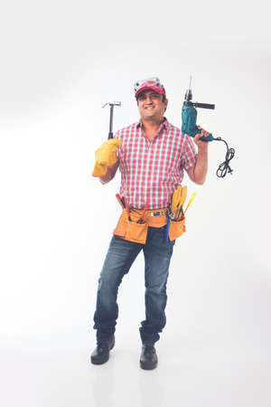 Indian electrician engineer in action with wire cutter, drilling machine etc, standing isolated over...