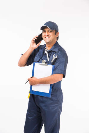 Indian happy auto mechanic in blue suit and cap holding spanner tool in action, isolated over white backgroundの写真素材