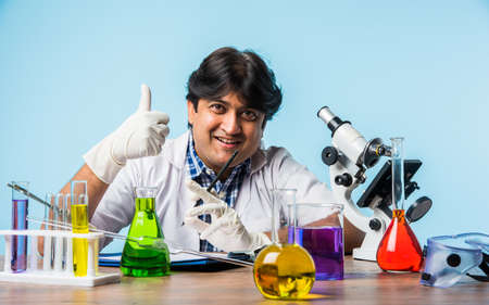Asian/Indian male scientist or doctor or science student experimenting with microscope and chemicals, laptop and smartphone in a labの写真素材