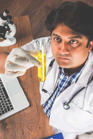 Asian/Indian male scientist or doctor or science student experimenting with microscope and chemicals, laptop and smartphone in a labの写真素材