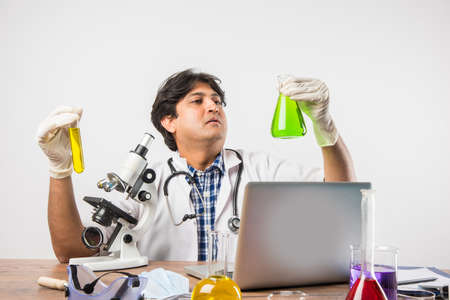 Asian/Indian male scientist or doctor or science student experimenting with microscope and chemicals, laptop and smartphone in a labの写真素材