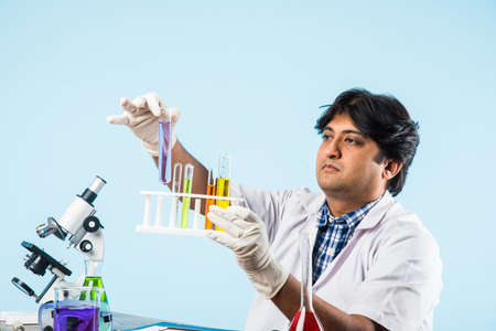 Asian/Indian male scientist or doctor or science student experimenting with microscope and chemicals, laptop and smartphone in a labの写真素材