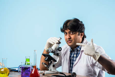 Asian/Indian male scientist or doctor or science student experimenting with microscope and chemicals, laptop and smartphone in a labの写真素材