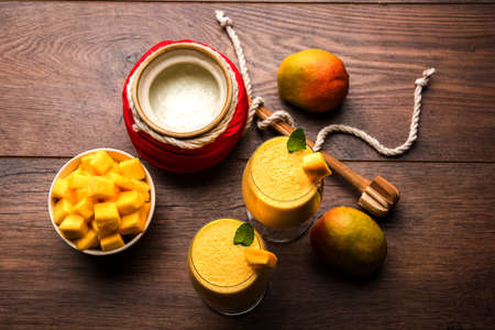 Mango Lassi or smoothie in big glass or small bottles with curd, cut fruit pieces and blender. Moody background, selective focusの写真素材