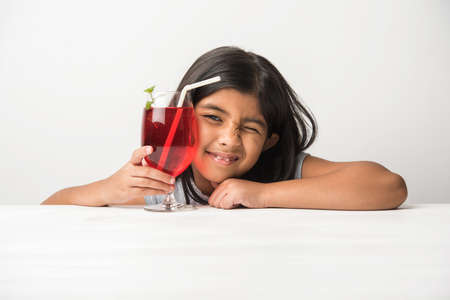 Cute asian/Indian little girl posing with cold drink or fresh juice at table over white backgroundの写真素材