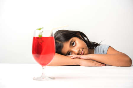Cute asian/Indian little girl posing with cold drink or fresh juice at table over white backgroundの写真素材
