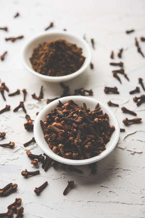 whole Cloves or laung or lavang with powder in a bowl isolated on white. Whole cloves. Selective...