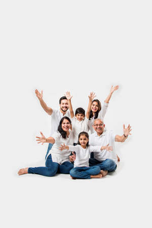 indian/asian family sitting over white background. senior and young couple with kids wearing white top and blue jeans. selective focusの写真素材