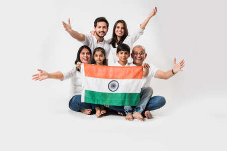 Happy Indian family holding national tricolour flag while sitting isolated over white background, selective focusの写真素材