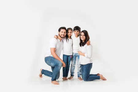 happy Indian family of 4 standing isolated over white background. Young couple with kids wearing white top and blue jeans. selective focusの写真素材