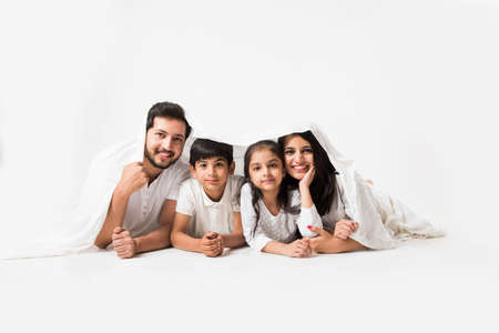 Indian parents with children lying under bed coverの写真素材